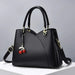 Black leather handbag with cherry charm and gold hardware on a white surface