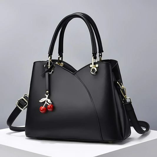 Black leather handbag with cherry charm and gold hardware on a white surface