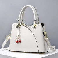 White leather handbag with gold hardware and cherry charm on neutral background