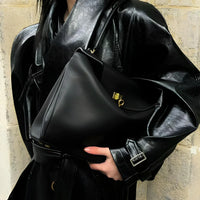 Woman in black leather coat holding a black leather handbag with gold hardware