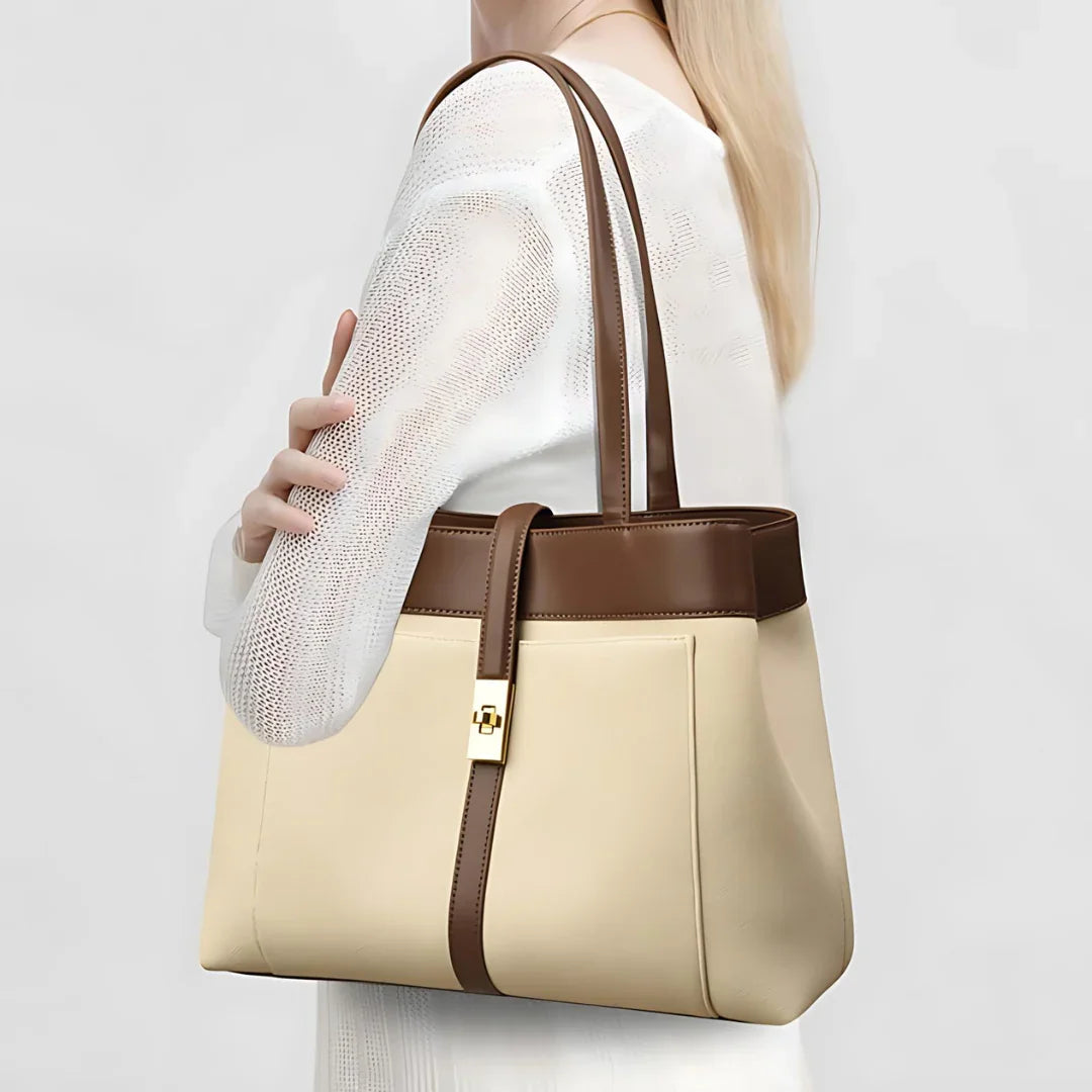 Woman holding a beige and brown leather tote bag with gold clasp, white outfit
