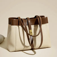 Beige canvas tote bag with brown leather trim and gold clasp on neutral background