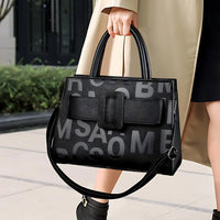 Woman carrying a black leather handbag with bold letter print, wearing trench coat