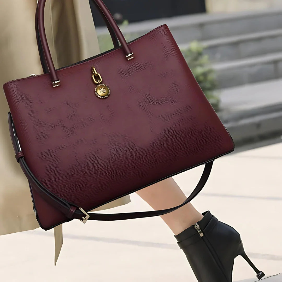 Woman holding burgundy leather handbag with gold charm, wearing black high heels