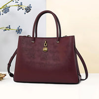 Burgundy leather tote handbag with gold pendant and shoulder strap on white background