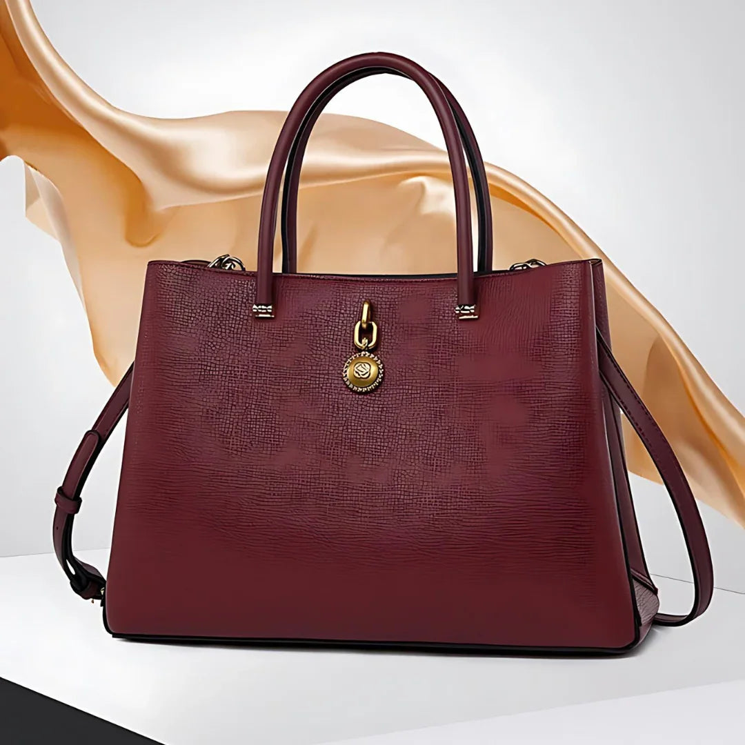 Elegant maroon leather handbag with gold charm on white and gold abstract background