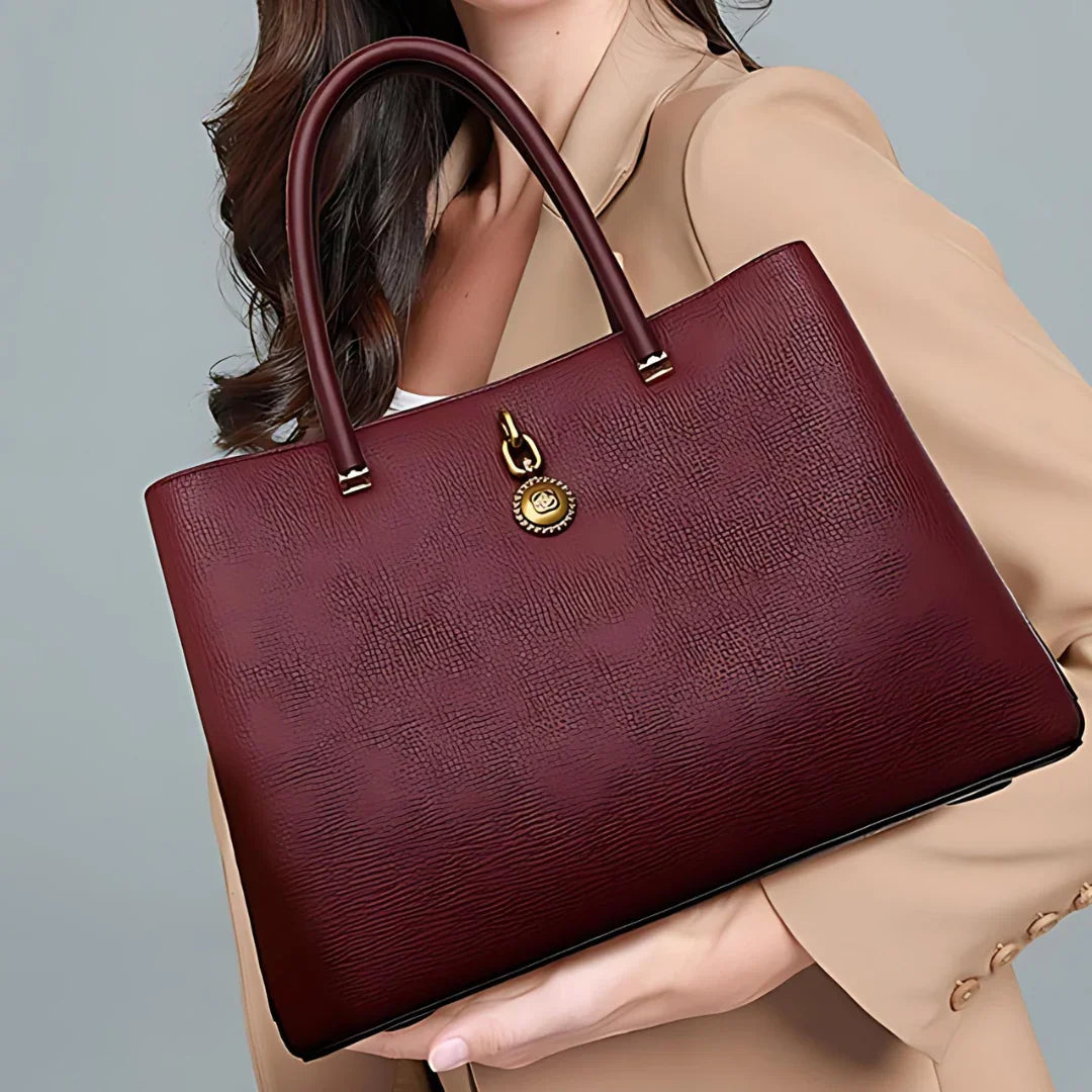 Woman in beige blazer holding textured burgundy leather handbag with gold hardware
