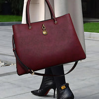 Woman holding large burgundy leather tote bag with gold hardware, wearing black heeled boots