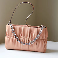 Peach ruched handbag with chunky silver chain strap on white table