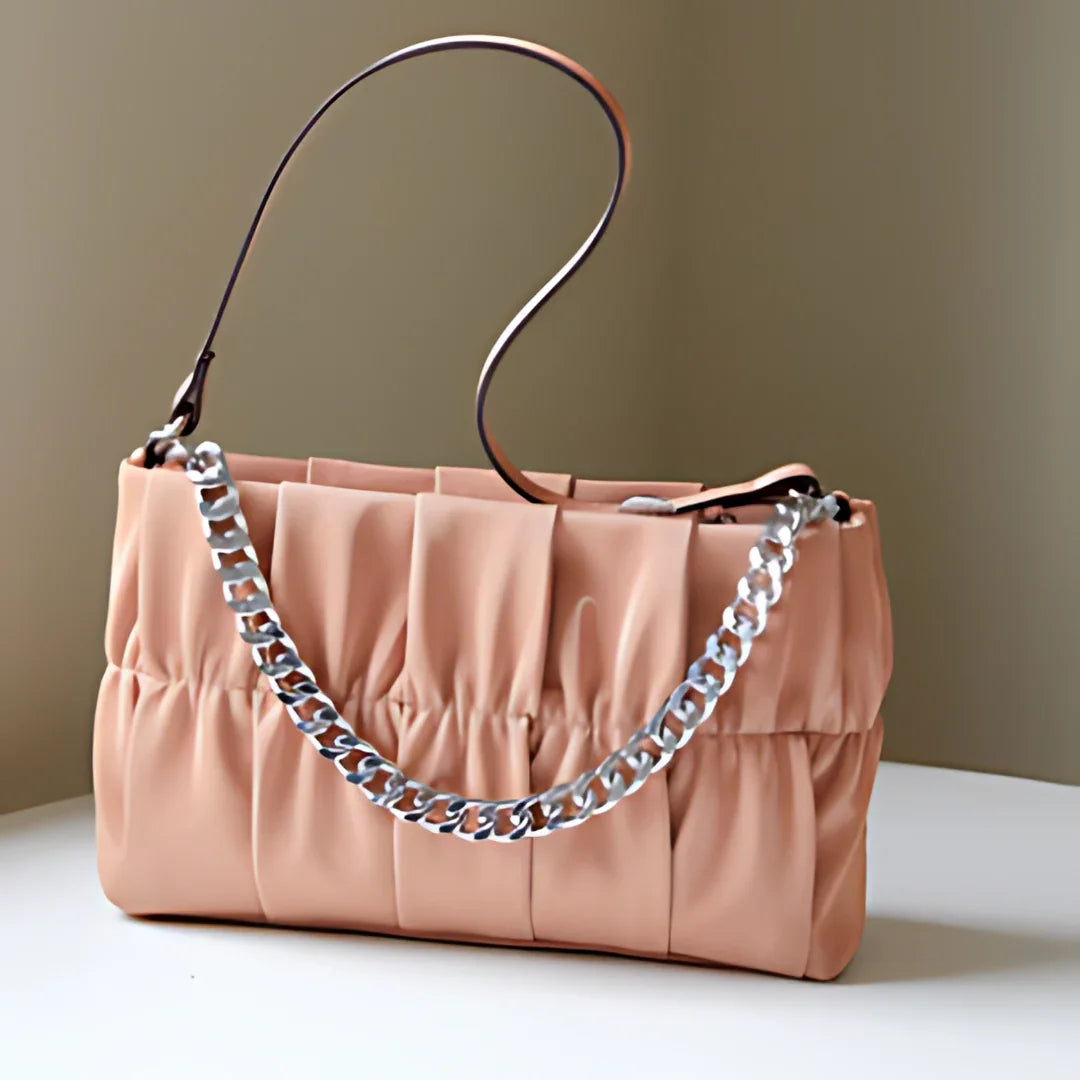 Peach ruched handbag with chunky silver chain strap on white table