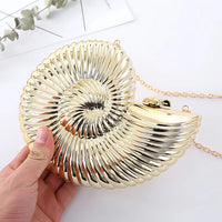 Gold seashell-shaped clutch handbag with chain strap held in hand on white background