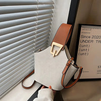 Modern white leather handbag with brown wide strap and gold buckle near window blinds
