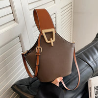 Brown leather bucket bag with gold buckle and adjustable strap on black sofa