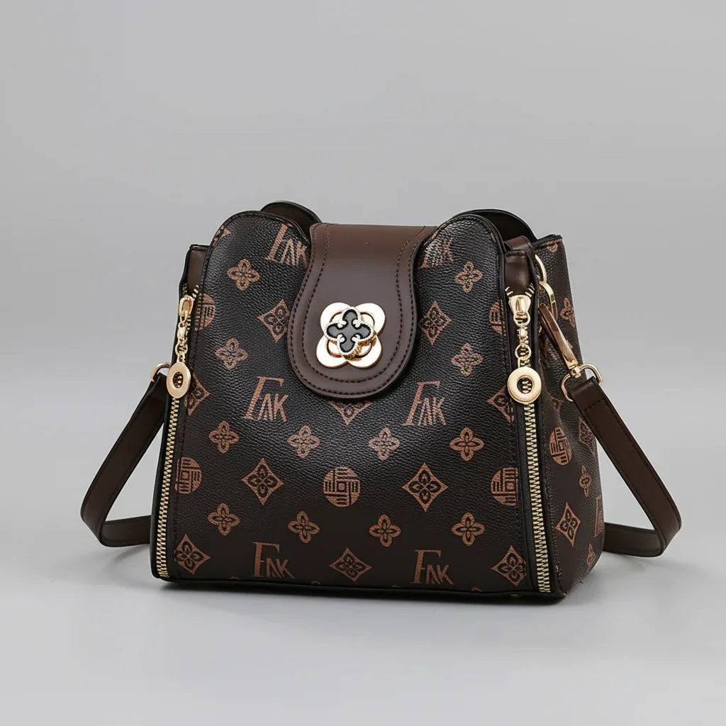 Brown patterned leather shoulder bag with gold accents and zipper details on gray background