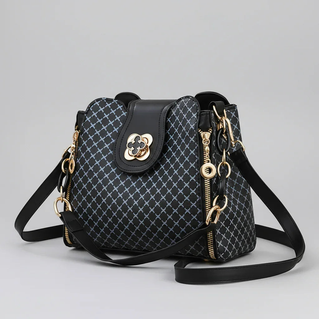 Black designer handbag with gold hardware, geometric pattern, and adjustable strap on gray background