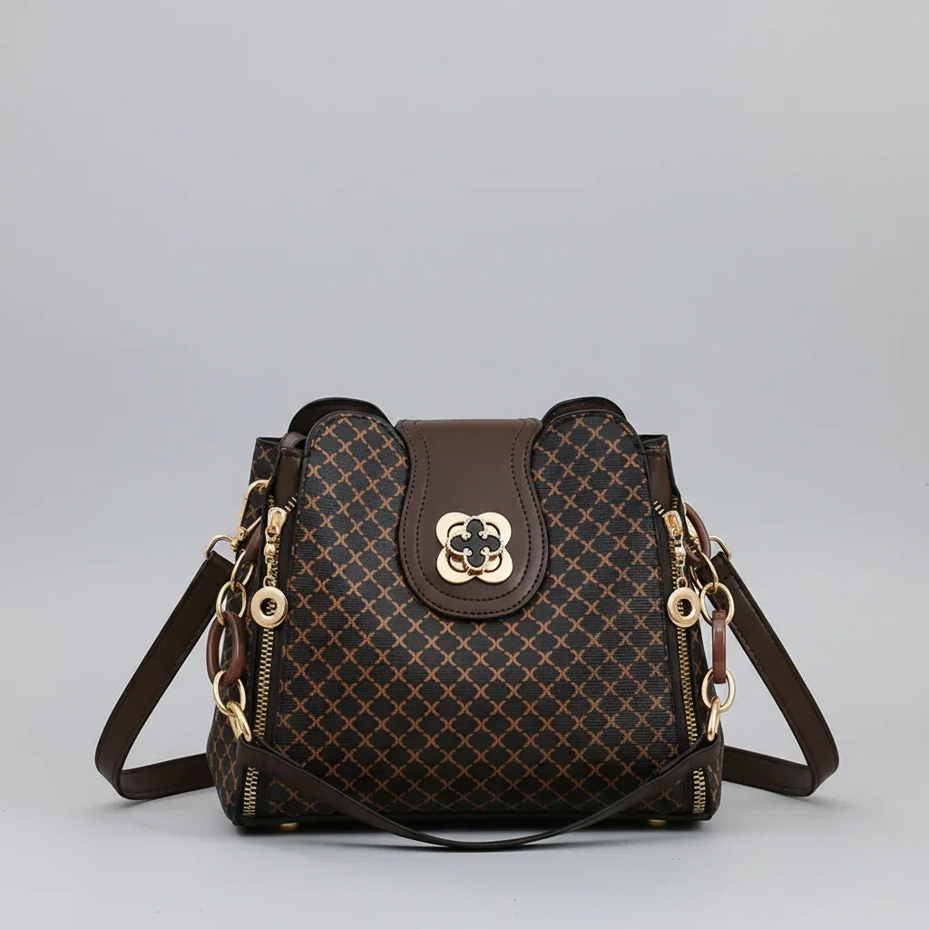 Brown patterned leather handbag with gold hardware and shoulder strap on gray background