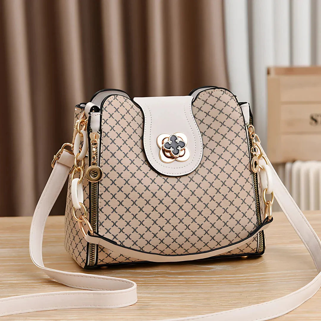 Beige designer crossbody bag with gold hardware, geometric pattern, and white strap on table