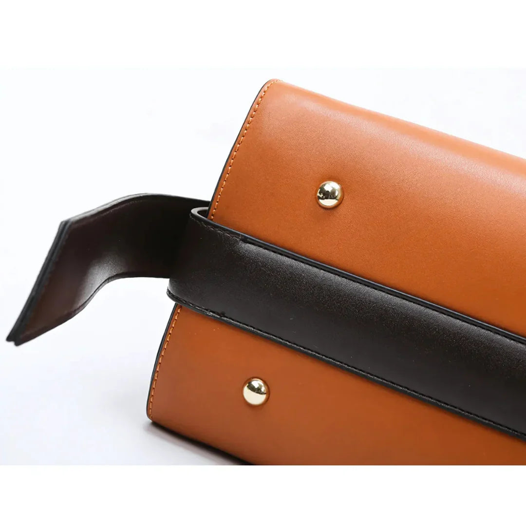 Brown leather handbag with black strap and gold studs on white background