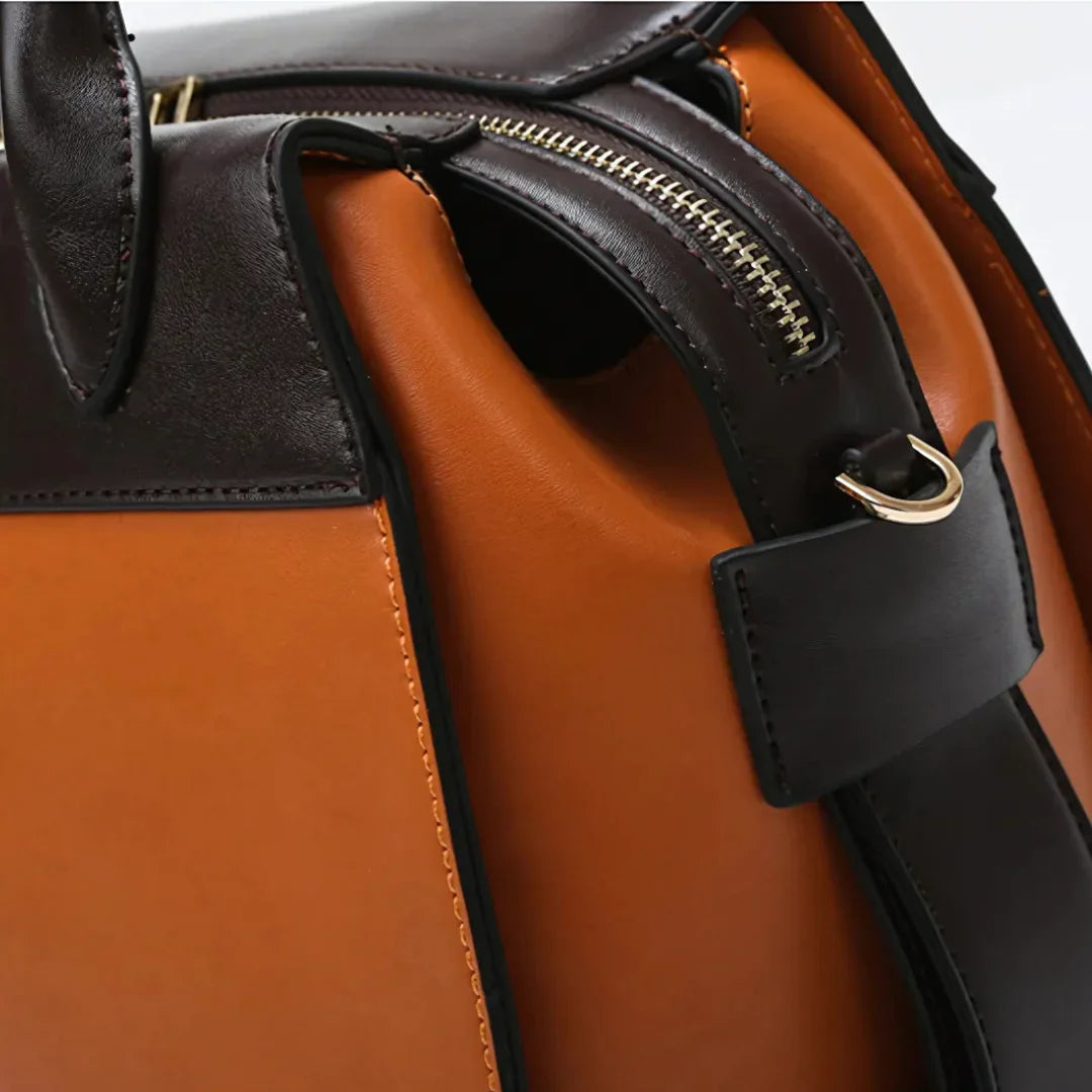 Brown and black leather handbag with gold zipper and metal accent close-up