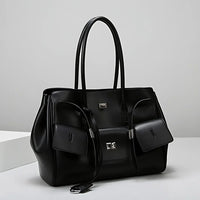 Black leather tote bag with silver hardware and two front pouches on a white surface