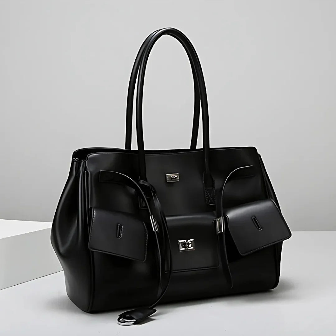 Black leather tote bag with silver hardware and two front pouches on a white surface