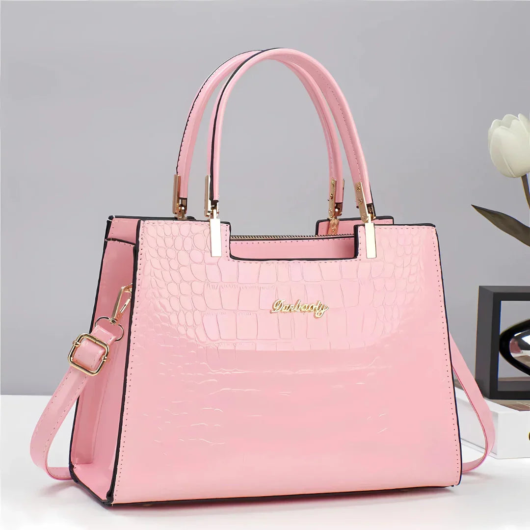 Pink crocodile-pattern faux leather handbag with gold hardware on white table