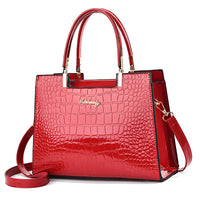 Glossy red crocodile pattern handbag with gold logo, top handles, and detachable strap