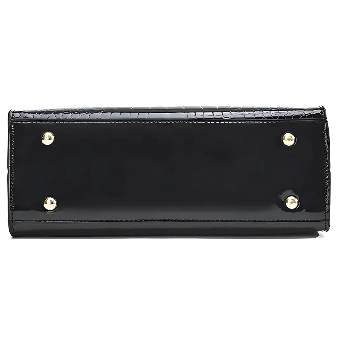 Bottom view of black patent leather handbag with gold metal feet and crocodile texture