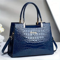 Glossy blue crocodile pattern handbag with gold accents on a white surface