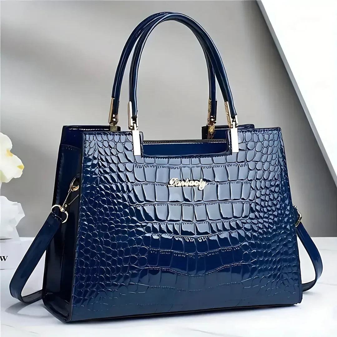 Glossy blue crocodile pattern handbag with gold accents on a white surface