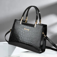 Black crocodile pattern handbag with gold hardware and dual handles on a white platform