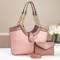 Pink crocodile-embossed handbag set with gold chain handles, wallet, and keychain on table