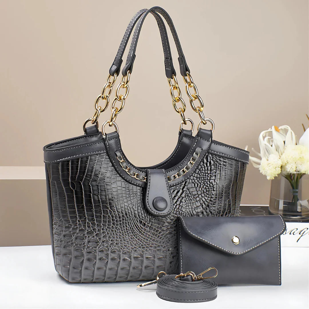 Black crocodile pattern leather handbag set with gold chain handles on white table
