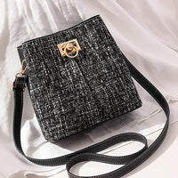 Black tweed crossbody bag with gold buckle and long adjustable strap on white fabric