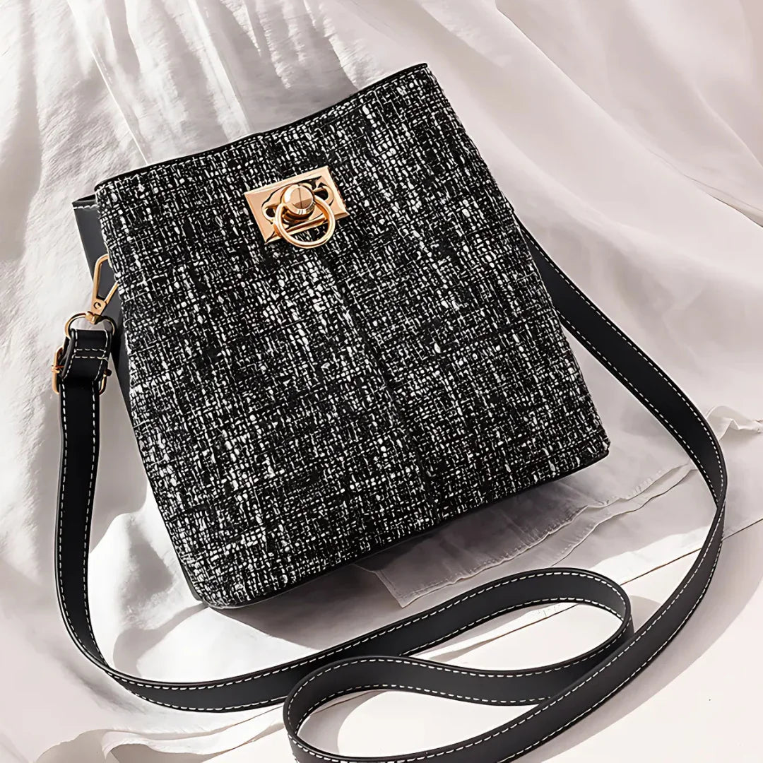 Black tweed crossbody bag with gold buckle and long adjustable strap on white fabric