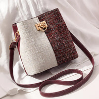 Two-tone textured bucket bag with gold clasp and burgundy strap on white fabric