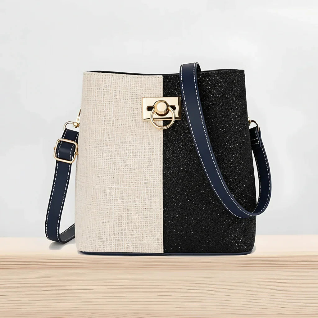 Two-tone bucket bag with gold hardware and navy strap on a wooden surface