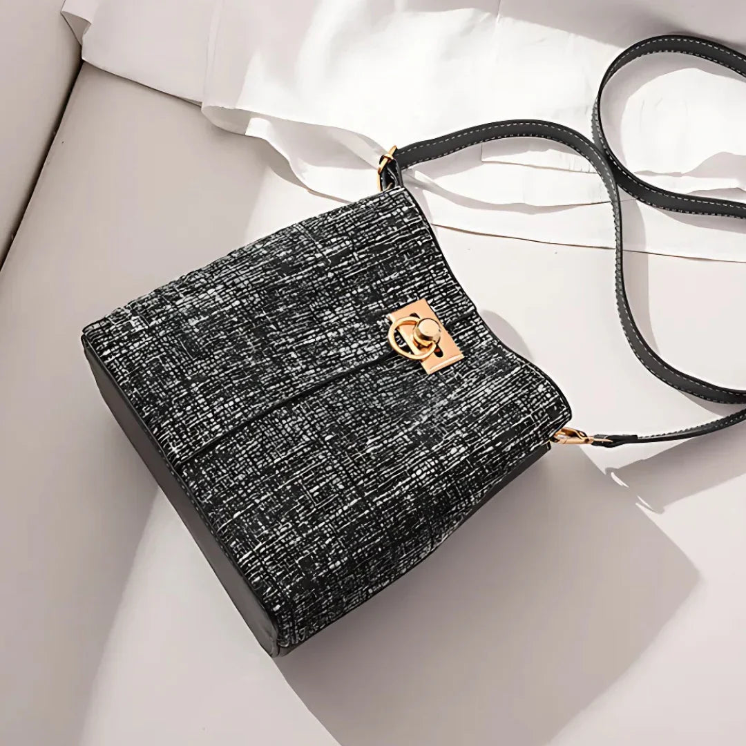 Black and white textured crossbody bag with gold clasp on a light background