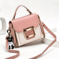 Pink and white handbag with gold buckle and bear keychain, crossbody strap