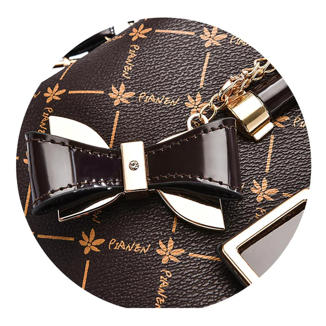 Brown designer handbag detail with gold bow charm and floral pattern