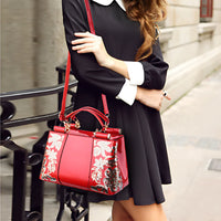 Woman in black dress holding shiny red floral handbag street style