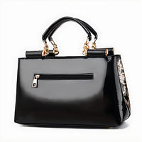 Glossy black handbag with gold chain handles and side floral sequin detail, front zipper