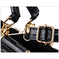 Close-up of a black patent leather handbag strap with gold buckle and hardware
