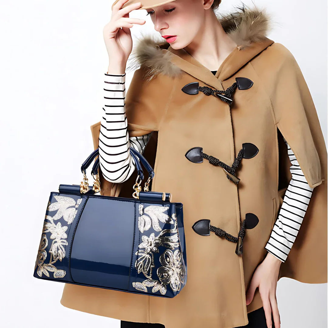 Woman in tan cape with fur trim holding blue handbag with gold floral embroidery