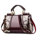Glossy maroon handbag with gold floral accents, double handles, and detachable strap