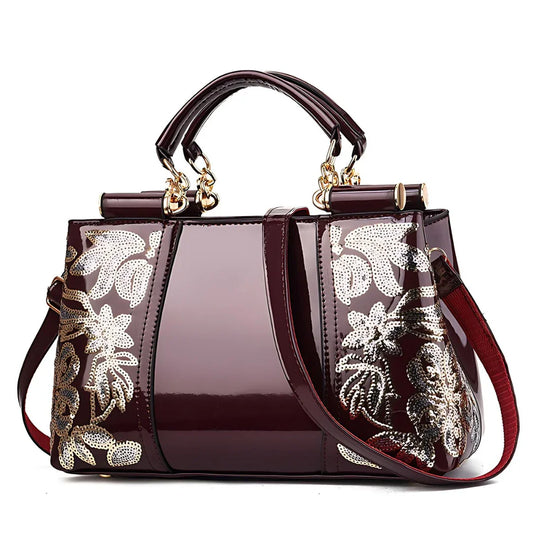 Glossy maroon handbag with gold floral accents, double handles, and detachable strap