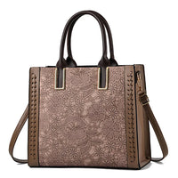 Brown floral handbag with lace pattern, leather accents, and gold hardware