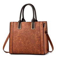 Brown leather handbag with floral embossing, double handles, and adjustable shoulder strap