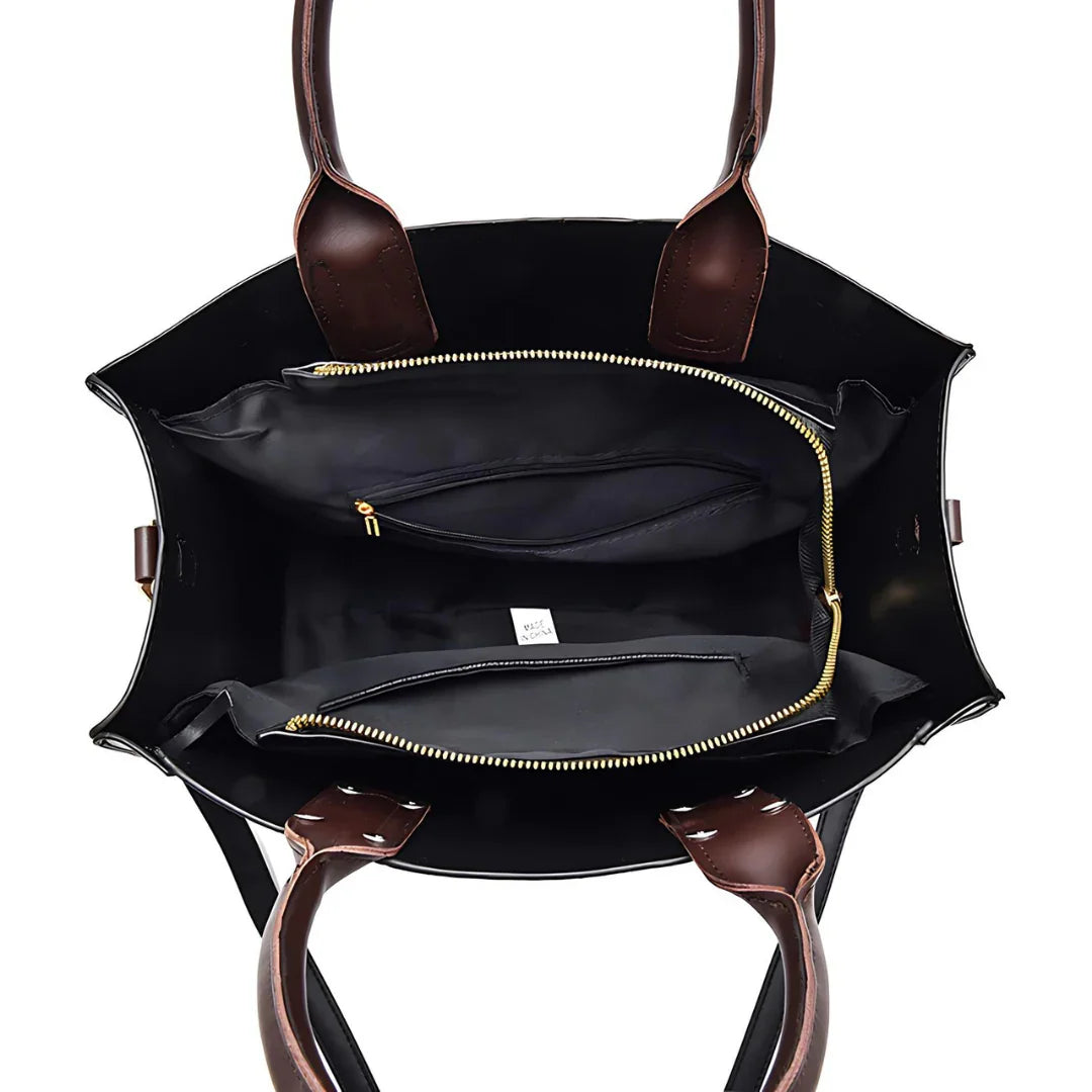 Open black tote bag with brown leather handles and gold zipper pockets