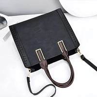 Black embossed leather handbag with gold accents and detachable strap on white background